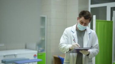 Maske takan ve beyaz önlüklü bir erkek sağlık görevlisi bir tıp dergisinin kapağına gergin bir şekilde bir şeyler yazıyor.