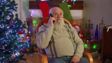 Noel 'de, Noel ağacının yanında bir koltukta otururken, yalnız yaşlı büyükbaba telefonda konuşuyor.