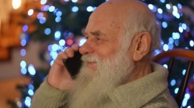 Yaşlı bir adam güzel, ışıl ışıl bir Noel ağacının arka planında cep telefonuyla hoş bir sohbet ediyor.