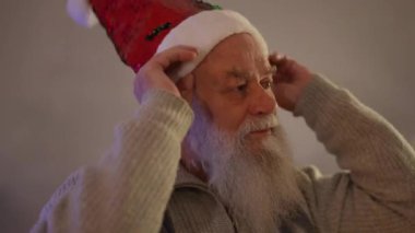 Yaşlı, kır saçlı, sakallı bir adam Noel şapkası takıyor.