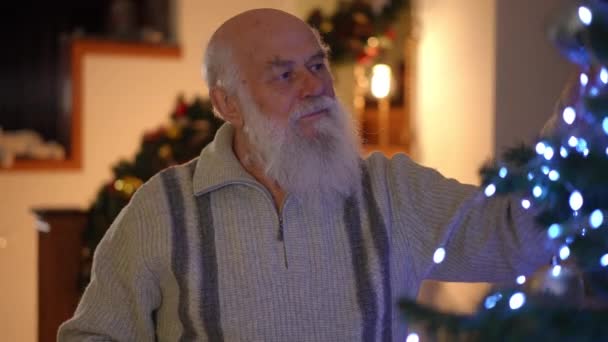Een Oudere Grijze Man Met Een Baard Versiert Een Kerstboom — Stockvideo