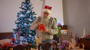 Sakallı ve Noel şapkası takan yaşlı bir adam Noel ağacının yanında duruyor. Bir adamın kravatını hediyesinden çıkarıp deniyor.