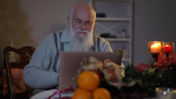 Siedząc Przy Świątecznym Stole Przy Świecach Starszy Brodaty Mężczyzna Pracujący — Wideo stockowe