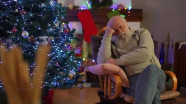 Yaşlı sakallı bir adam süslü bir Noel ağacının yanındaki sallanan sandalyede uyuyakaldı.