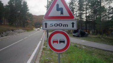 Kırmızı bir araba, bir dağ yolu boyunca yüksek hızda ilerliyor. İleride keskin bir dönüş olduğunu gösteren bir tabelanın yanında ve 500 metre boyunca geçmek yasaktır..