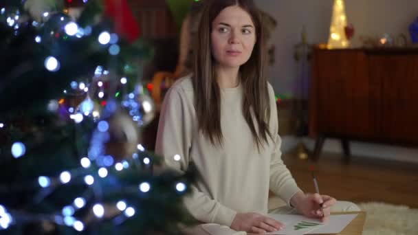 妊娠中の女性は 蓮の位置にクリスマスツリーの近くに座っている間描いています クリスマスと新年の前夜のレジャー — ストック動画