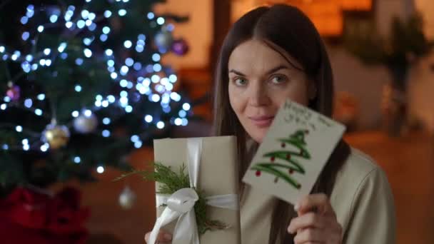 女性は 白いリボンで飾られた贈り物が新年のカードでどのように調和的に見えるかを示しています 手作りの贈り物からのポジティブな感情 — ストック動画