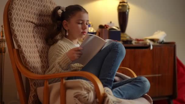 Een Meisje Leest Een Fascinerend Boek Terwijl Een Schommelstoel Zit — Stockvideo