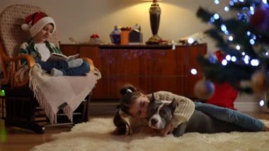 Noel 'de çocuklar için boş zaman. Kitaplı sallanan sandalyede oturan çocuk, köpekli Noel ağacının yanındaki kız.
