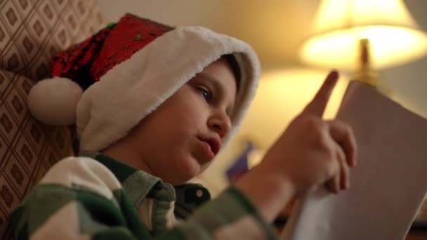 Chłopiec Świątecznym Kapeluszu Siedzi Bujanym Krześle Czyta Książkę Zbliżenie — Wideo stockowe