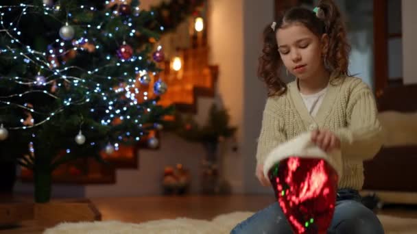 Ένα Κορίτσι Κάθεται Στο Χαλί Κοντά Ένα Χριστουγεννιάτικο Δέντρο Δοκιμάζει — Αρχείο Βίντεο