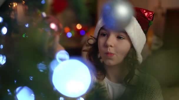 Zbliżenie Dziewczyna Świątecznym Kapeluszu Starannie Wybiera Świąteczne Kulki Choince — Wideo stockowe