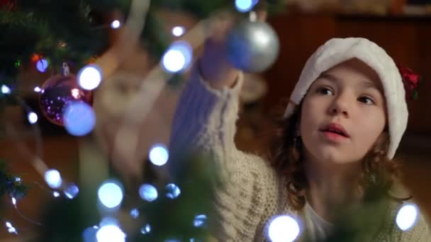 Ένα Κορίτσι Χριστουγεννιάτικο Καπέλο Κρεμάει Μια Ασημένια Μπάλα Ένα Χριστουγεννιάτικο — Αρχείο Βίντεο
