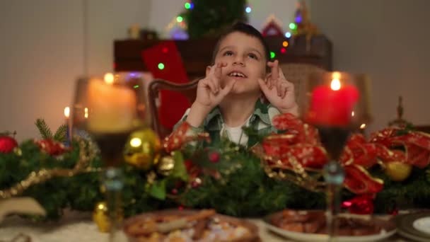 Мальчик Сидя Празднично Украшенным Столом Рождество Загадывает Желания Закрытыми Глазами — стоковое видео