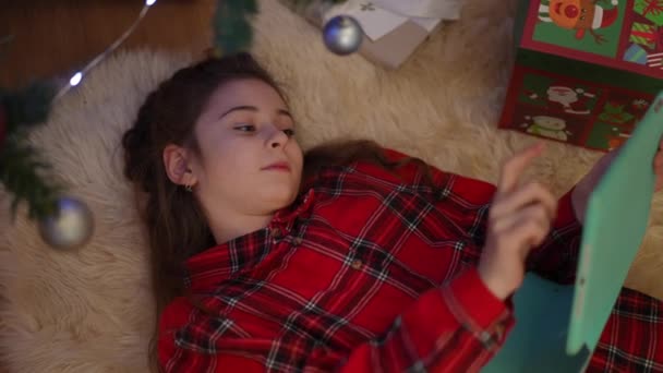 圣诞早晨的和谐慢动作 一个女孩躺在圣诞树旁的一块石碑旁玩着一个圣诞球 — 图库视频影像
