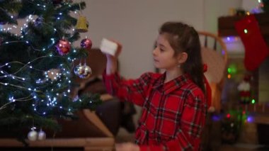 Bir kız Noel ağacında bulunan hediyeyi açıyor. Noel hediyesinin lezzeti