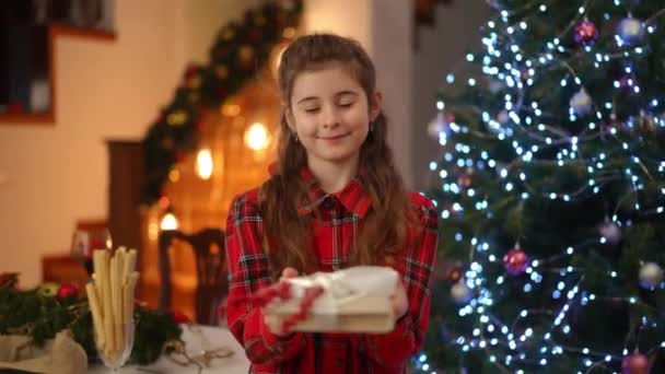 Стоячи Біля Ялинки Усміхнена Дівчина Тримає Обидві Руки Подарунок Який — стокове відео