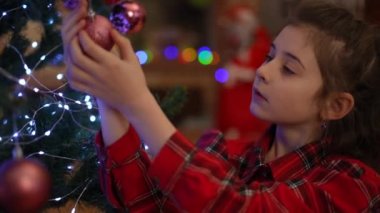 Noel ağacında bir Noel balosunun pırıltısı. Bir kızın elleri modern bir evde Noel için süslenmiş.