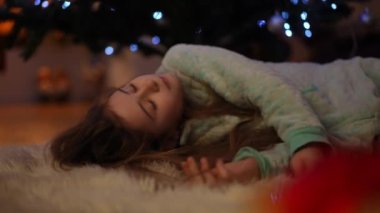 Ağır çekim. Noel 'i bekliyorum. Kız Noel ağacının yanındaki halıda bayramı beklerken uykuya daldı.