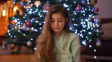 Noel 'i bekliyorum. Noel ağacının arka planında pijamalı bir kız bayramın gelmesini beklemekten yoruldu.