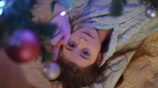 Dziewczyna Leży Dywanie Obok Choinki Bawi Się Świąteczną Piłką Wiszącą — Wideo stockowe