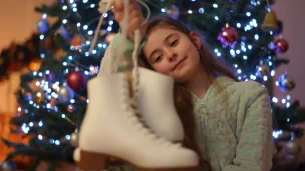 一个穿着睡衣的漂亮女孩坐在圣诞树旁 手里拿着溜冰鞋 她笑着 盼望着滑冰 — 图库视频影像