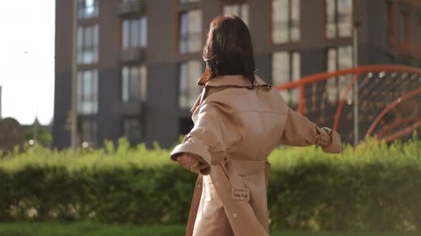 一位穿着时尚的年轻女子在一个现代住宅区的公园区的背景下旋转着 看着摄像机 — 图库视频影像