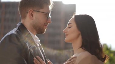 Ağır çekim. Yakın plan. Gözlüklü bir adam ve güzel bir kadın binaların arka planına bakıyorlar. Sonra adam nazikçe kadını alnından öper.