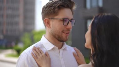 Ağır çekim. Omzundan vuruluyor. Yakın plan. Bir kadın iki koluyla bir erkeğe sarılır. Adam gülümser ve kameraya bakar.
