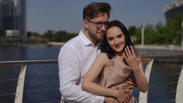 一对快乐的夫妇拥抱在一起 站在城堤上看着摄像机 一个微笑的女人把戒指戴在她的手指上 建立一个新的家庭 — 图库视频影像