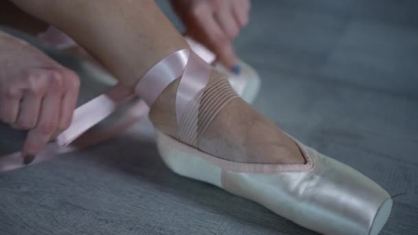 在一位坐在木制地板上的芭蕾舞演员脚上放尖鞋的过程中的一个特写镜头 — 图库视频影像