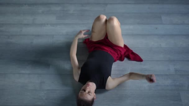 在舞厅的木制地板上 俯瞰着一位躺着的芭蕾舞演员的全景 她的膝盖弯了 双腿紧贴着她 — 图库视频影像