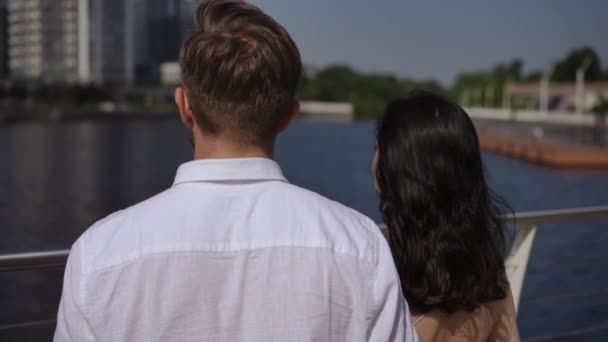 这对夫妇站在河堤上 背对着摄像机 凝视着河对岸的城市 女人看着心爱的人 把头靠在他的肩上 — 图库视频影像