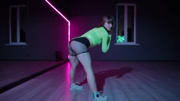 ライブカメラ ネオン照明と暗い振付ホールで明るい段階の衣装で美しい若い女の子によって実行されたTwerk — ストック動画