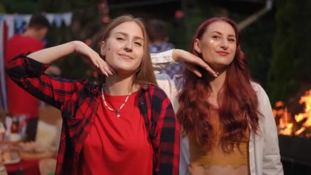 バーベキューの友人の会社の2人の女の子は カメラのためにポーズし 笑顔を浮かべ カメラにキスを吹きます アウトドアパーティーの友人 — ストック動画