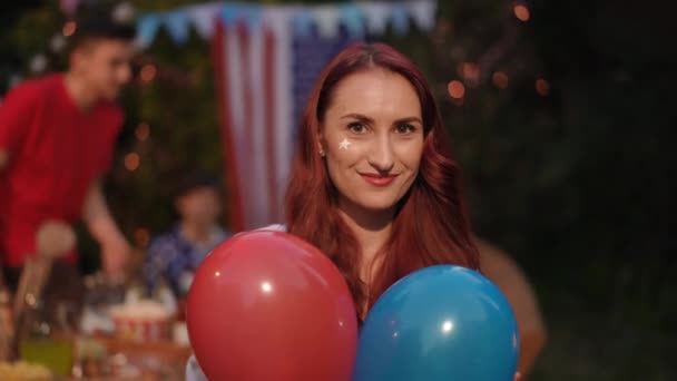 クローズアップ 少女は赤と青の風船を投げ カメラを見ながら微笑んでいる 友人の会社での独立記念日 — ストック動画