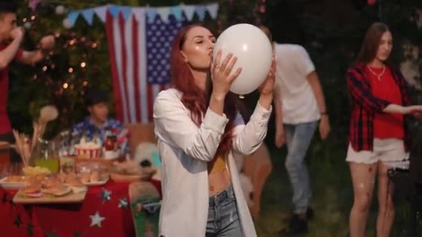 女の子は白い風船にキスし それを投げ 屋外の友人の会社のバーベキューでカメラで微笑んでいるように見えます 7月4日 独立記念日 — ストック動画