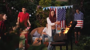 Arkadaşlarla birlikte ateşin yanında iki mutlu kızın şefkatle kucaklaşması. Bağımsızlık Günü Barbeküsü.