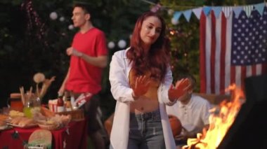 Kız kendisi ve arkadaşı için şişe su getiriyor. Kızlar akşam ateşin etrafında, arkadaşlarıyla birlikteler. Bağımsızlık Günü Barbeküsü.