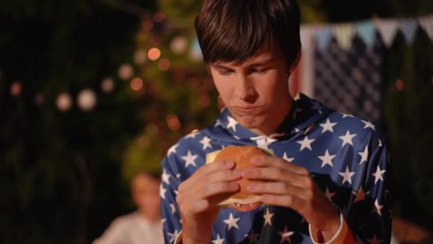 クローズアップ ティーンエイジャーは屋外で友達とパーティーでハンバーガーを食べる 男は彼が食べていたハンバーガーの味を高く評価しました — ストック動画