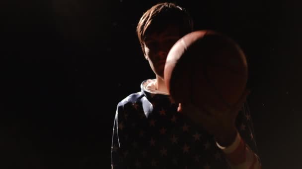 クローズアップ スターストライプの服のティーンエイジャーは 火の光の中で暗闇に立っている間 彼の手にバスケットボールで遊びます — ストック動画