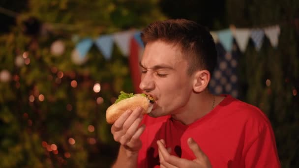 クローズアップ 男はホットソーセージで美味しいホットドッグを食べ 自然の中で自分の手で準備しました 屋外パーティーで友達とストリートフード — ストック動画