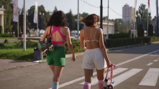 Két Barátnő Görkorcsolyát Hordoz Kezében Miközben Sétálnak Egy Városi Parkban — Stock videók