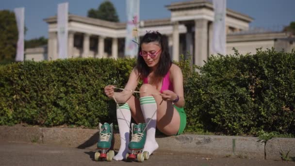 一个戴着眼镜的年轻女子 在阳光灿烂的日子里 坐在城市公园里新鲜的空气中 把溜冰鞋放在她的腿上 女孩笑了 — 图库视频影像