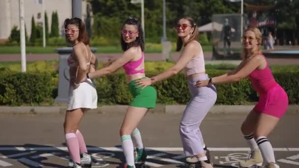 ライブカメラ ローラースケートの4人の若い女性は晴れた日に都市公園でユニゾンに移動しようとします — ストック動画
