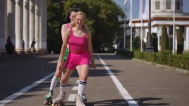 Güneşli bir günde güneş gözlüklü iki kız şehir parkında paten kayıyor. Aktif eğlencenin neşe ve kahkahası. Yavaş çekim