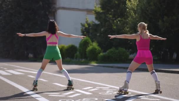 ローラースケートの2人の若い女性は 晴れた日に街の公園でゆっくりとした動きでダンスの動きを示しています — ストック動画