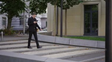 Koyu takım elbiseli şık bir genç adam iş toplantısına gidiyor. Bir iş adamı cep telefonuyla bir arama yapar. Geniş, dalgalı adımlarda yürürken..