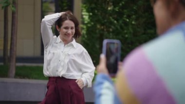 Kadın cep telefonuyla fotoğraf çektirmek istedi ve başarılı bir çekim için farklı şekillerde poz verdi. Omzunun üstünden ateş ediyorlar.