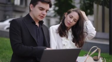 Bir erkek, şehirdeki bir bankta otururken bir kadına dizüstü bilgisayarıyla nasıl düzgün çalışacağını öğretir. Kadın bir not defterine soruyor ve yazıyor..